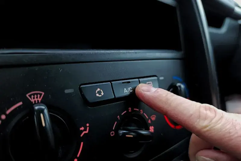 Driver pressing the A/C button on a car climate control panel