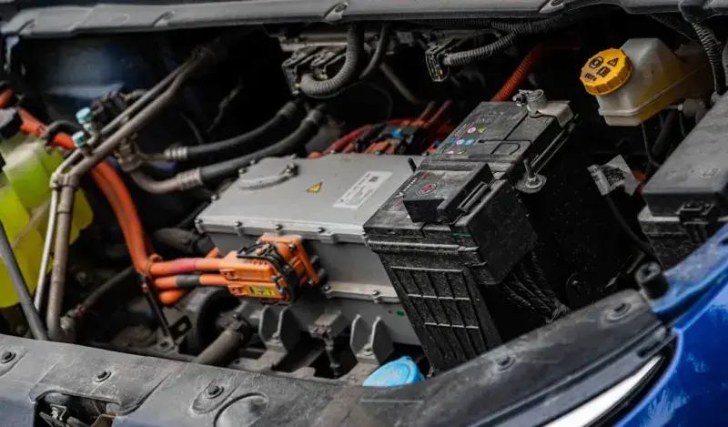 Electric vehicle engine bay showing orange high-voltage cabling and the 12-volt battery