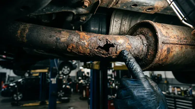 Close-up of a rust hole in a corroded exhaust pipe under a raised car at FastLane Mechanics in Mississauga